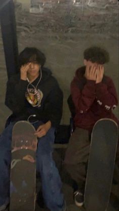 two young men sitting next to each other with their skateboards in front of them