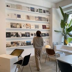 a woman standing in front of a white wall filled with pictures and books on it