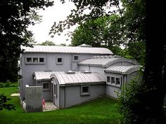 a large gray building sitting in the middle of a lush green field next to trees