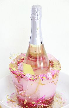 a bottle of champagne sitting on top of a cake covered in pink and gold sprinkles