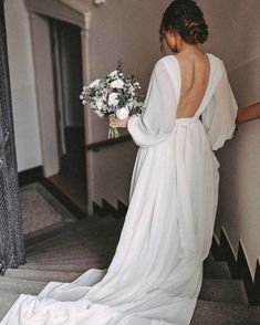 a woman in a white dress is walking down the stairs with her back to the camera