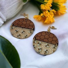 two wooden earrings with honeycombs and bees on them sitting next to yellow flowers