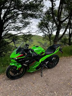 a green and black motorcycle parked on the side of a dirt road next to trees