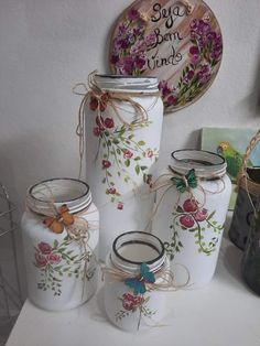 four jars with flowers painted on them are sitting on a table next to a plate