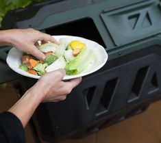 a person holding a plate with vegetables on it in front of a trash can,