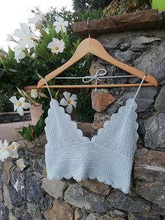 a blue knitted bralet hanging on a wooden hanger next to a stone wall