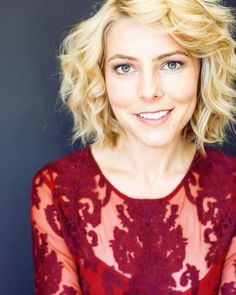 a woman with blonde hair and blue eyes wearing a red dress smiling at the camera