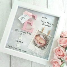 a baby's birth announcement in a frame with pink flowers on the table next to it