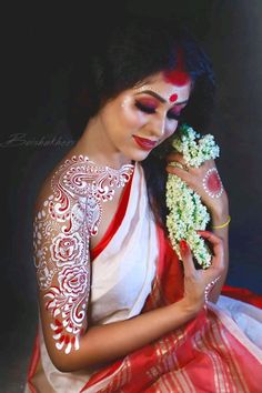 a woman with white and red makeup is holding flowers in her hands, while sitting down