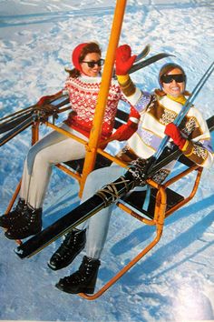 two people sitting on a ski lift in the snow wearing skis and holding ski poles