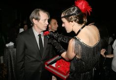 a man in a suit talking to a woman in a black dress at a party