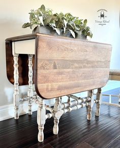 a wooden table sitting on top of a hard wood floor next to a potted plant