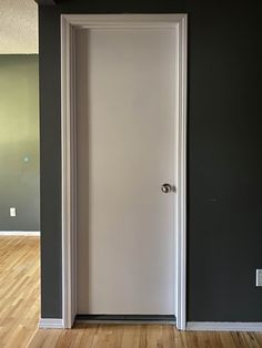 an empty room with a white door and hard wood flooring on the side wall