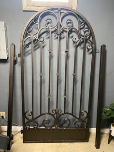 an ornate iron bed frame in the corner of a room with blue walls and a potted plant next to it