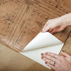 two hands are holding a piece of paper on top of a wooden table with an ornate design