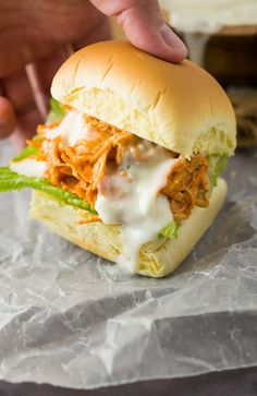 a hand is picking up a pulled pork sandwich from a wrapper on wax paper