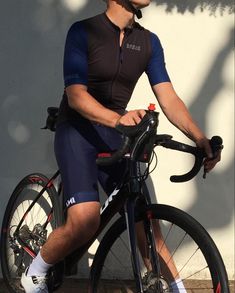 a man riding on the back of a bike next to a white wall and tree