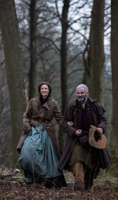 an older man and woman walking through the woods