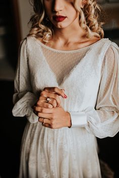 a woman wearing a white dress and holding her hands on her chest while standing in front of a window