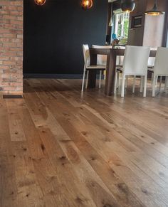 a dining room with wood floors and white chairs in front of a brick wall that has two pendant lights hanging from the ceiling