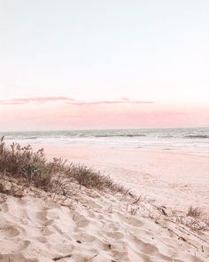 a surfboard sitting on top of a sandy beach next to the ocean at sunset