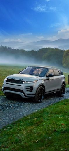 a white range rover parked on the side of a dirt road next to a field