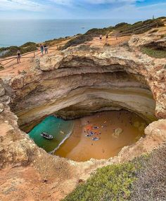 people are standing on the beach near an ocean cave with a small boat in it