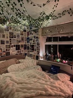 an unmade bed with lots of pictures on the wall and lights hanging from the ceiling