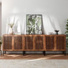 a wooden sideboard in front of a painting and potted plants on the floor