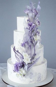 a three tiered wedding cake with purple and white flowers