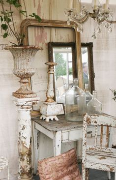 an old table with two chairs and a vase on it next to a mirror in a room