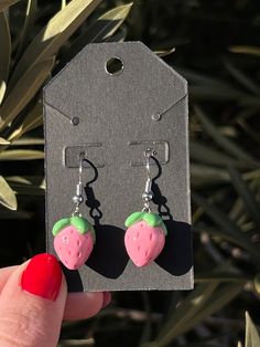 a pair of pink and green strawberry shaped earrings on a black tag with red nail polish