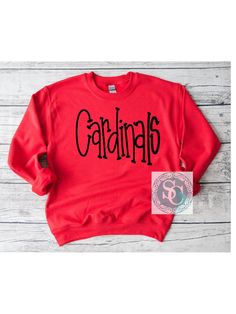 These Cardinals handwritten shirts are a perfect addition to your school spirit wear and are super cozy!  ❗️Sizes: Toddler-2T-5T  Youth XS-XL  Adult S-XL  Adult 2X Adult 3X Available in short sleeve, long sleeve and sweatshirts!  Shirts are all unisex sizing!  The shirt has cardinals printed and pressed onto the shirt! Cardinals is written in black!  If you would like to request a custom order, please send us a message!! Cardinals School Spirit Shirts, Cardinals Spirit Wear, Cardinal School Spirit Shirts, Casual School Tops For Sports Season, Casual Tops For School Sports Season, School Fan Apparel Sweatshirt With Letter Print, Fall School Sweatshirt With Team Name, Casual Tops With Lettering For Fan Gear, Casual Tops With Fan Gear Lettering