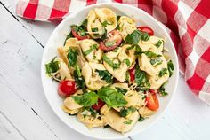 a white bowl filled with pasta and veggies on top of a checkered table cloth