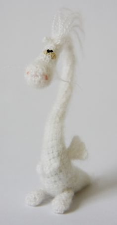 a crocheted white dragon sitting on its hind legs with it's head turned to the side