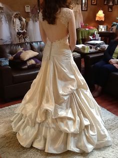 a woman in a wedding dress is looking at herself in the mirror while another person sits on a couch