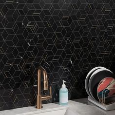 a kitchen sink with black and gold tiles on the wall behind it, next to a white dishwasher