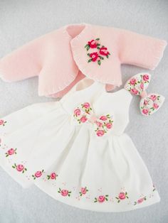 the doll is wearing a white dress with pink flowers on it and has a matching hat