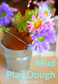 a metal bucket filled with purple flowers on top of a wooden table and the words mud play dough in front of it