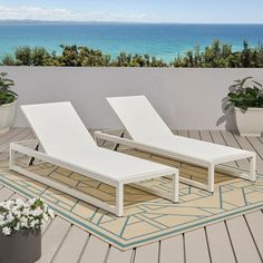 two white lounge chairs sitting on top of a wooden deck next to the ocean with potted plants