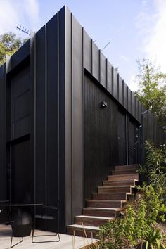 a black house with stairs leading up to it's entrance and patio area, surrounded by greenery