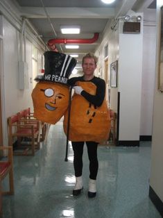 a woman is walking down the hallway with two pumpkins on her head and holding a sign that says mr peanut