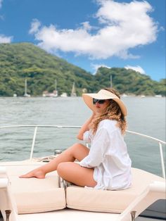 a woman sitting on the back of a boat wearing a white shirt and sun hat