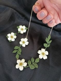 a hand holding a necklace with white flowers on it and green leaves attached to the chain