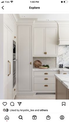 a kitchen with marble counter tops and white cabinets, along with brass pulls on the doors