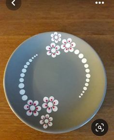 a plate with flowers painted on it sitting on top of a wooden table next to a cell phone