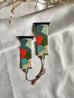 two pairs of colorful earrings sitting on top of a white cloth covered table next to dry grass