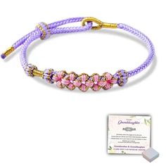 a purple bracelet with pink flowers and gold beads on it, next to a card