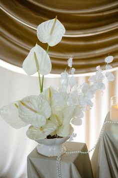 white flowers are in a vase on a table with pearls and beaded curtains behind it