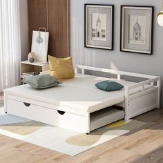 a white bed frame with drawers underneath it in a living room next to two pictures on the wall